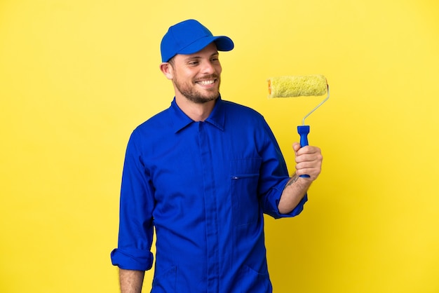 Painter Brazilian man isolated on yellow background looking to the side and smiling