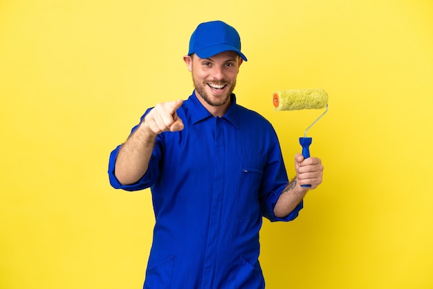 Painter Brazilian man isolated on yellow background surprised and pointing front