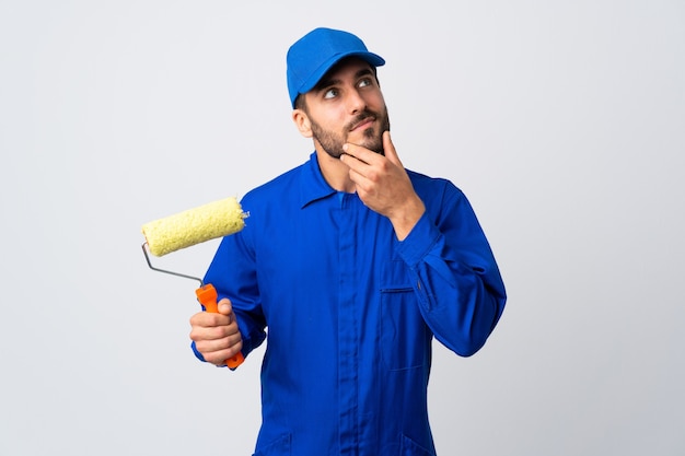 Painter man holding a paint roller isolated on white background having doubts