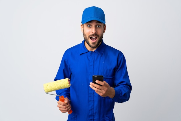 Painter man holding a paint roller isolated on white background surprised and sending a message