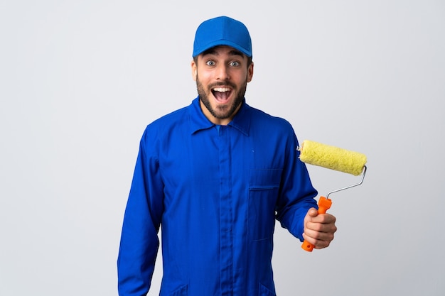 Painter man holding a paint roller isolated on white background with surprise facial expression