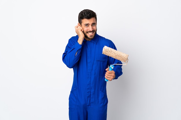 Painter man holding a paint roller isolated on white frustrated and covering ears