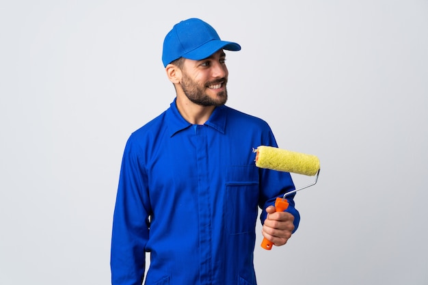 Painter man holding a paint roller isolated on white looking to the side and smiling