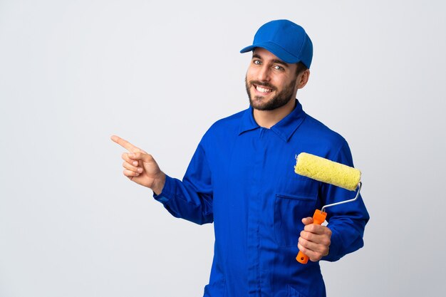 Painter man holding a paint roller isolated on white pointing finger to the side