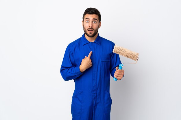 Painter man holding a paint roller isolated on white pointing to oneself