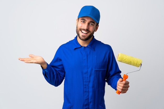 Painter man holding a paint roller isolated on white wall holding copyspace imaginary on the palm to insert an ad