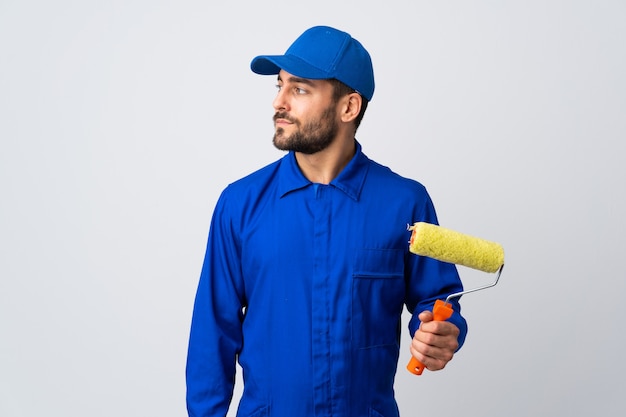 Painter man holding a paint roller isolated on white wall looking to the side