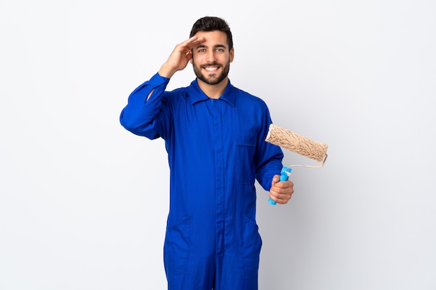 Painter man holding a paint roller isolated on white wall saluting with hand with happy expression