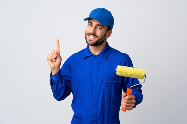 Painter man holding a paint roller isolated on white wall showing and lifting a finger in sign of the best