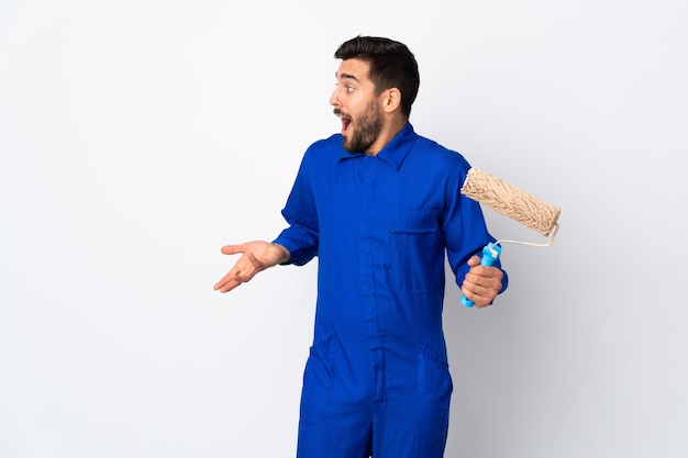 Painter man holding a paint roller isolated on white with surprise expression while looking side