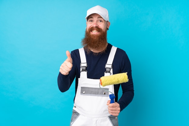 Painter man with long beard over isolated blue wall giving a thumbs up gesture