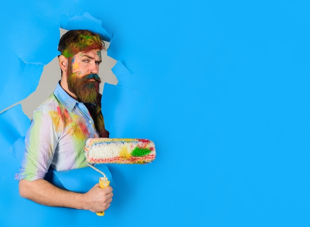 Painter painter with painting roller through hole in paper\
handsome bearded worker with paint roller