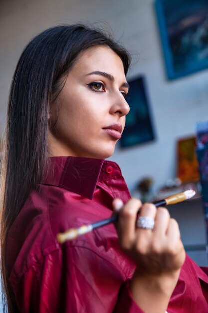 Photo painter paints with watercolors in workshop at home portrait of pretty young woman artist in art studio and painting on canvas