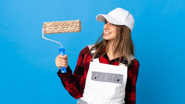 Painter woman over isolated blue background looking to the side and smiling