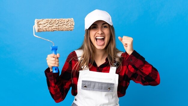 Painter woman over isolated blue wall celebrating a victory in winner position