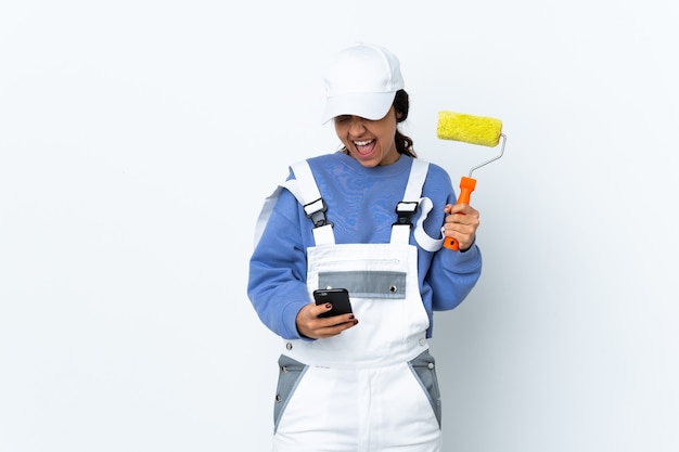 Painter woman over isolated white wall with phone in victory position