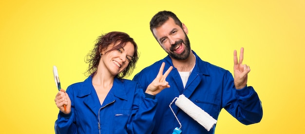 Painters smiling and showing victory sign with both hands on colorful background