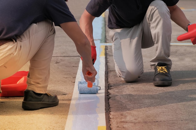 Painters working together painting blue lines striping on floor of parking lots in the car park