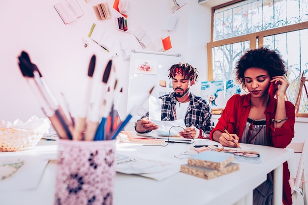 Painting brushes. Interior designers sitting at the table with many papers and painting brushes