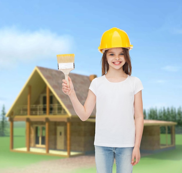 painting, building, childhood and people concept - smiling little girl in protective helmet with paint brush