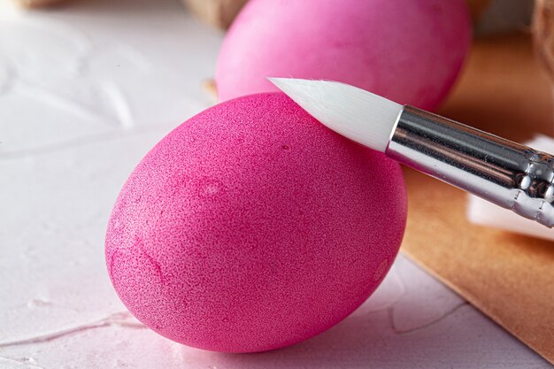 Painting Easter eggs in pink on white table, view from above