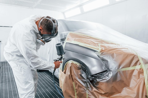 Painting job in progress Caucasian automobile repairman in uniform works in garage