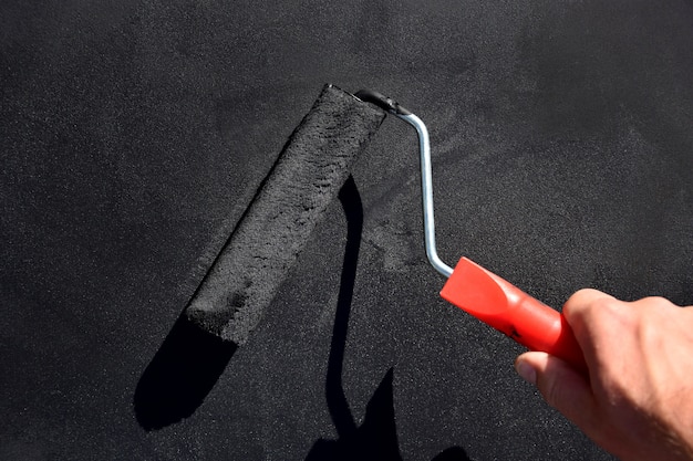 painting the surface in black with a brush roller.man's hand holds brush roller.