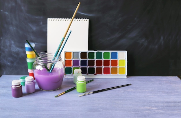 Paints borstels water op een houten tafel tegen de achtergrond van een schoolbord terug naar school