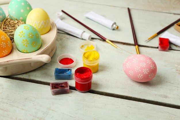 Paints and brushes with Easter eggs on wooden table