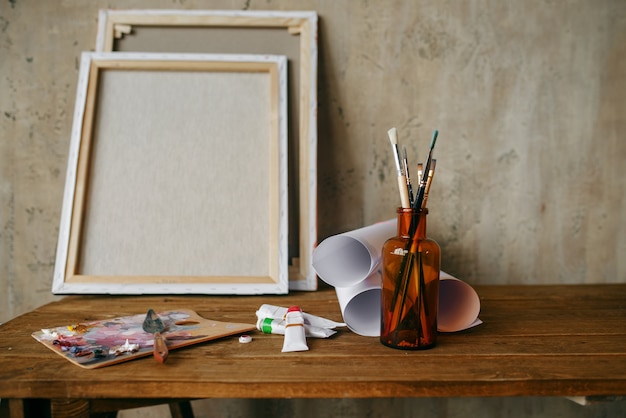 paints on palette, brush in bottle, canvas, nobody. painter tools on the table in art studio, equipment on artist workplace, paintbrush