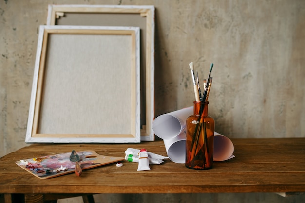 Paints on palette, brush in bottle, canvas, nobody. Painter tools on the table in art studio, equipment on artist workplace, paintbrush