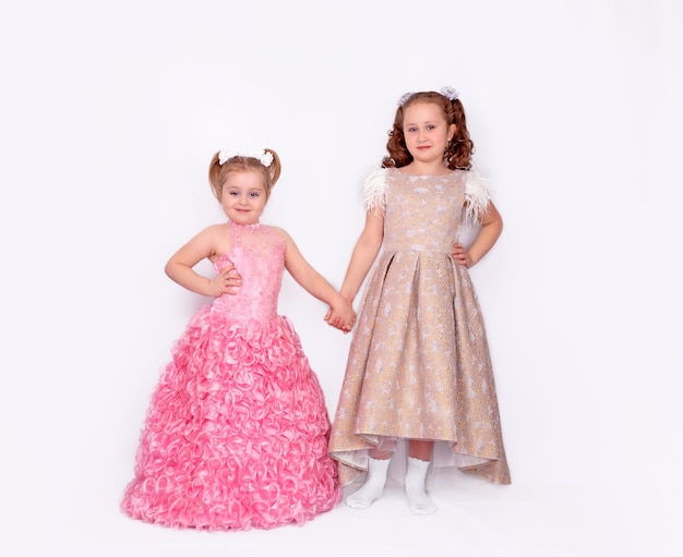 A pair of adorable little girls in ball gowns isolated on a white background.