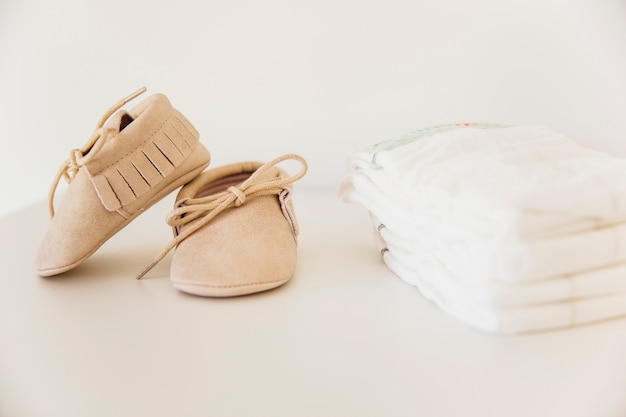 Pair of baby shoes and stacked of diaper on beige background