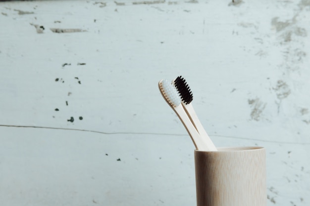 A pair of bamboo toothbrushes over a white wooden