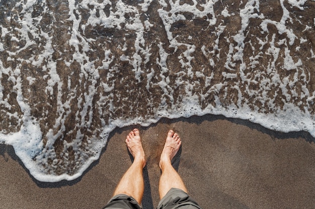 잔잔한 파도에 부분적으로 잠긴 검은 모래 위에 단단히 박힌 한 쌍의 맨발