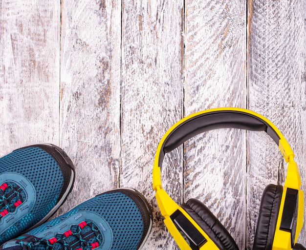 Pair of blue women sneakers and yellow headphones on white wooden background