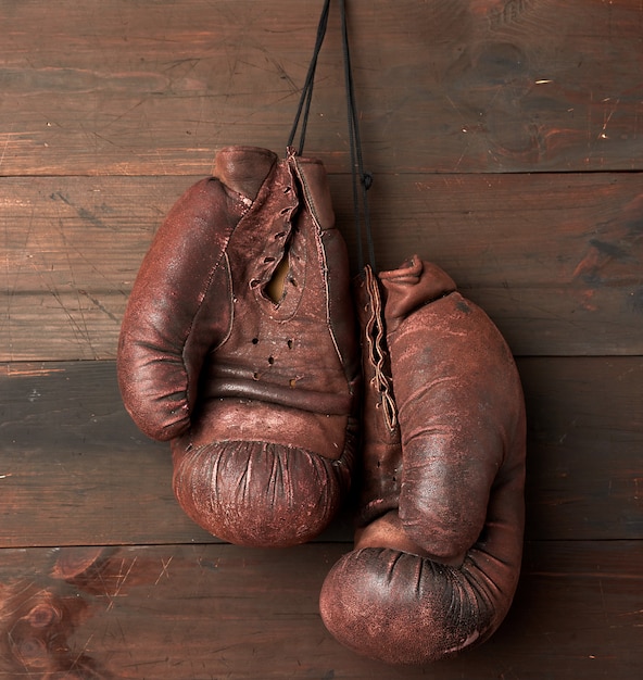 Paio di guantoni da boxe in pelle marrone appesi su una parete di legno