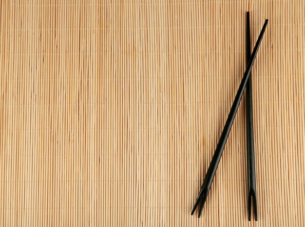 Photo pair of chopsticks on light bamboo mat background