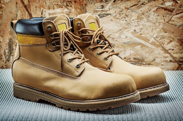 Pair of classic leather working boots close up view on background of plywood