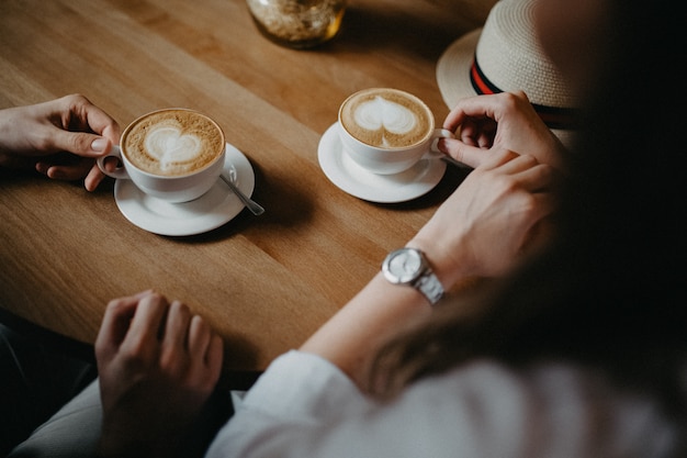 Pair of coffee cups with hearts drawn with hands of couple