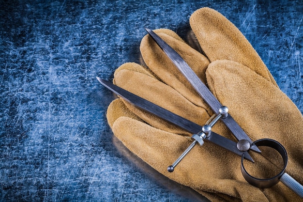 Photo pair of construction compasses leather protective gloves on metallic background