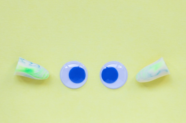 Pair of earplug and eyes on the yellow background Good sleep and noise protection concept