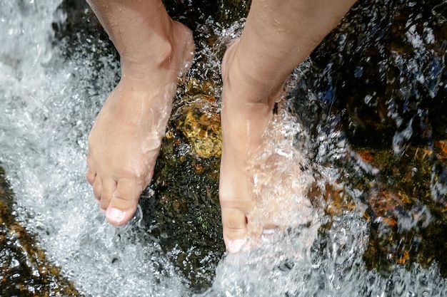 Pair of feet of a woman at waterfall getting wet with water