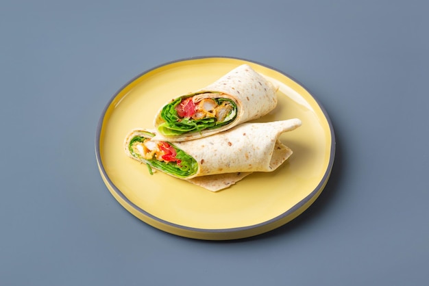 Pair of fresh wrap sandwiches with chicken and vegetables on yellow on grey plate trendy color high ...