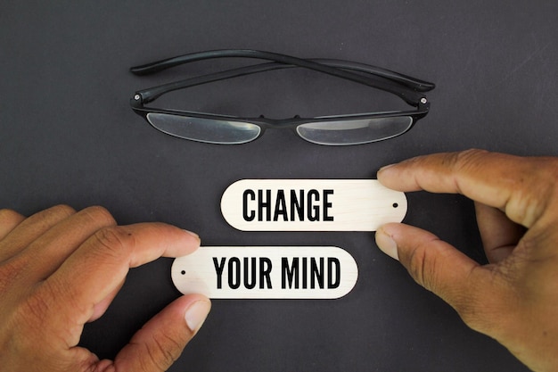 A pair of glasses are next to a person holding a change your mind tag.