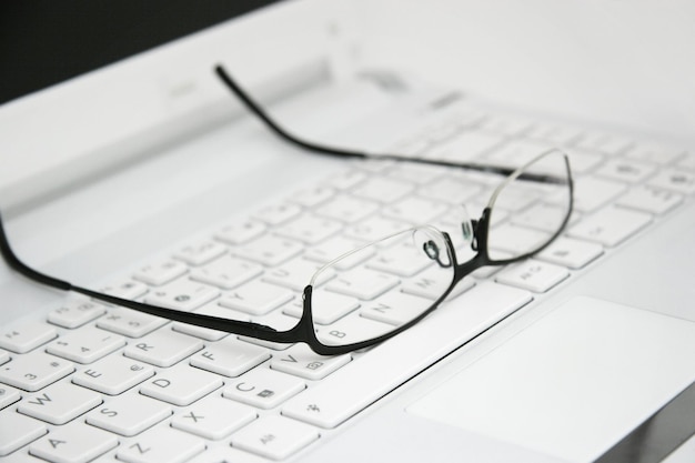 A pair of glasses are on a white computer keyboard