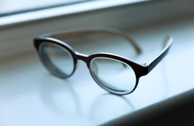 A pair of glasses on a window sill with the word reading on it.