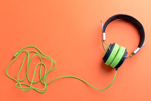 A pair of greenblack headphones on orange background