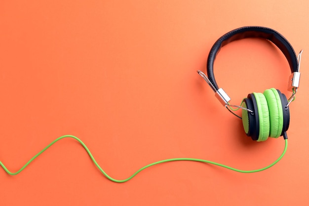 A pair of greenblack headphones on orange background