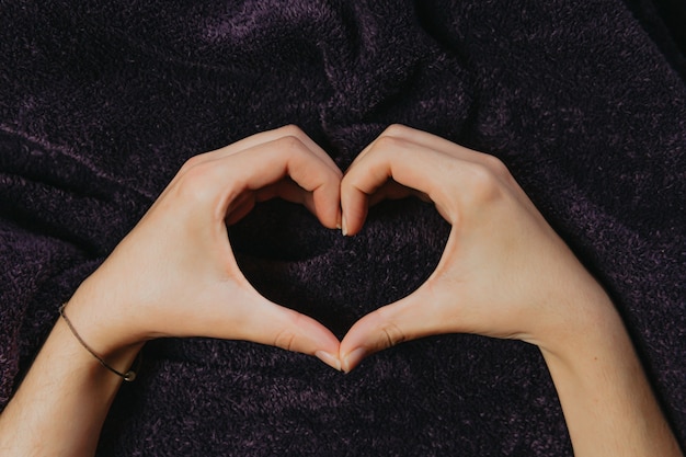 Foto un paio di mani che fanno un cuore sopra una coperta viola